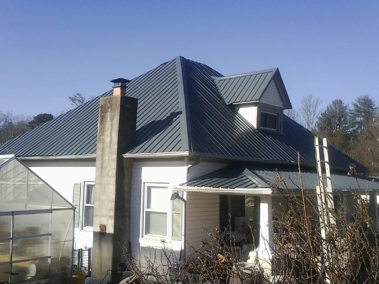 Dark blue standing seam metal roof on a white farmhouse with dormer — Slate & Tile Roof Repair by Roofing Brothers in Owatonna