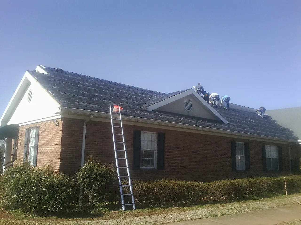 Crew tearing shingles off a brick ranch roof with a ladder set — Emergency Roof Repair work by our crew in Owatonna