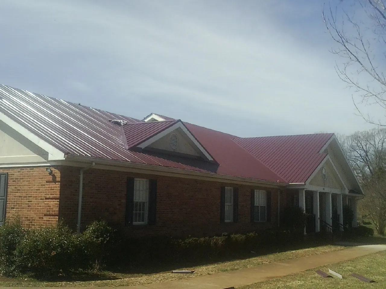 Red metal roof with gabled entries on a long brick building, from a Hail Damage Roof Repair job in Owatonna