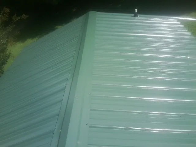 New green metal panels meeting at the ridge of a roof — Flat Roof Repair work by our crew in Owatonna