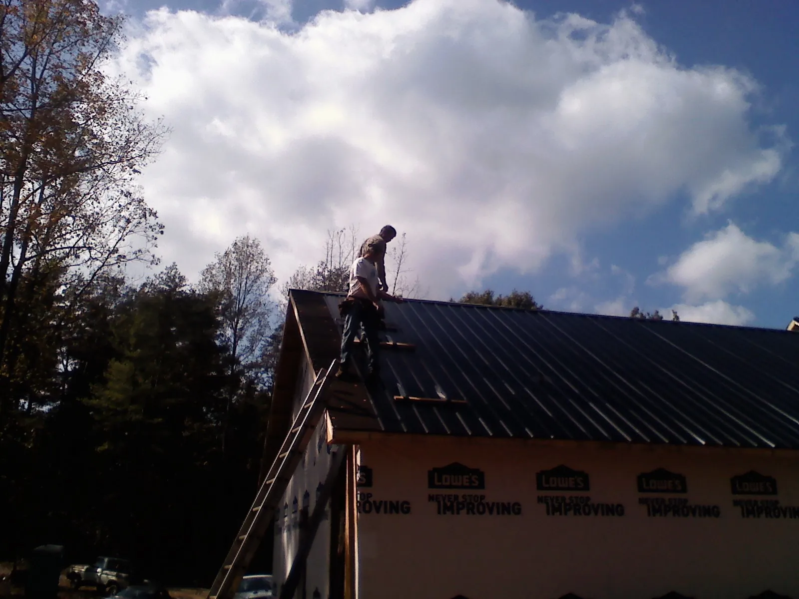 Roofer fastening dark metal panels high against a cloudy sky, from a Roof Inspection job in Owatonna