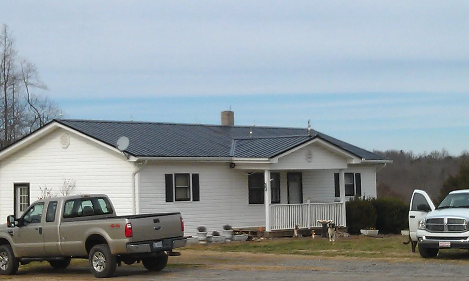 Finished dark metal roof on a white ranch home with work trucks parked in Owatonna