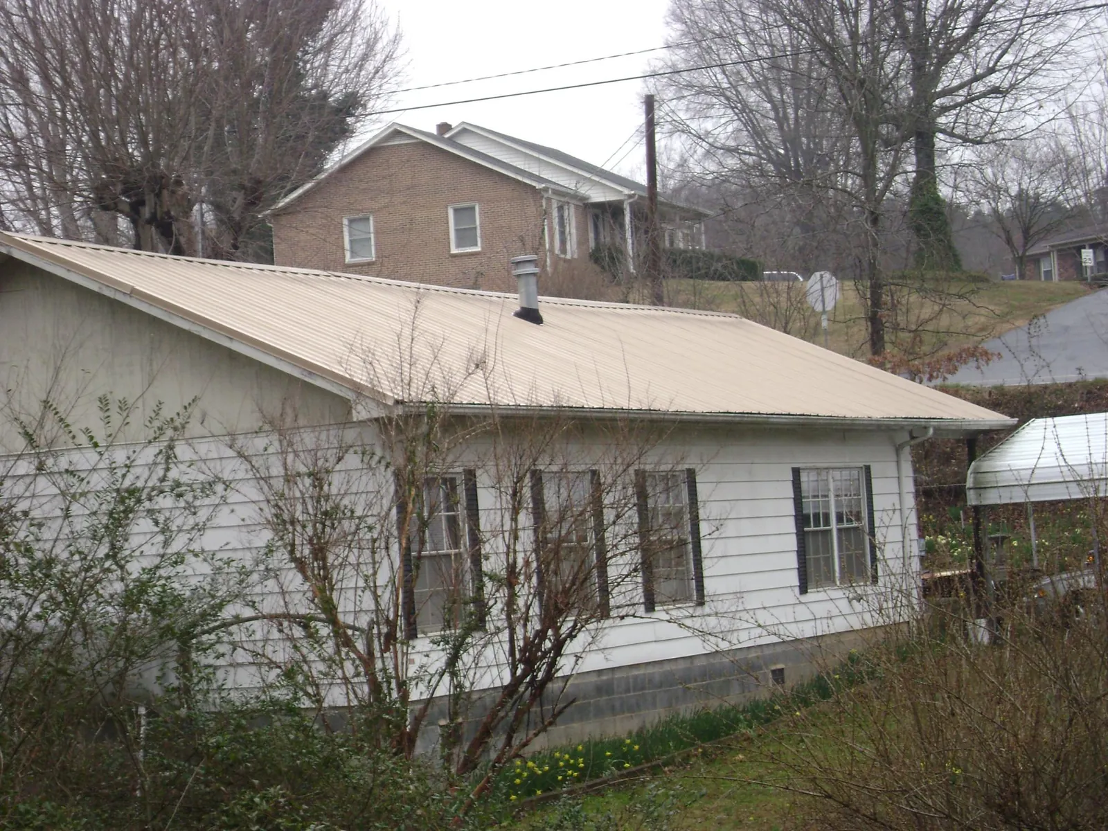 Tan metal roof on a white sided house set into a hillside — Commercial Roofing by Roofing Brothers in Owatonna